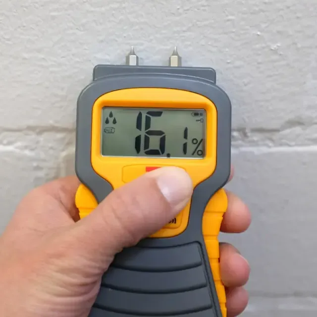 A pin moisture meter checking a wet wall during a water damage inspection