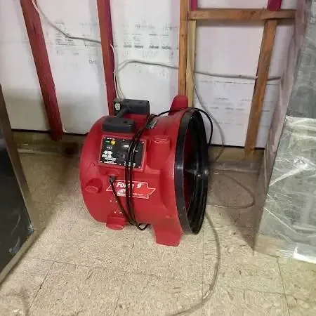 Water damage restoration in Anoka: a red air mover and plastic sheeting by an opened lower wall