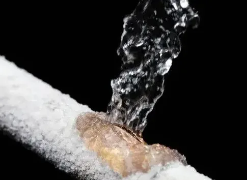 A frost-covered pipe split open and spraying after a hard freeze