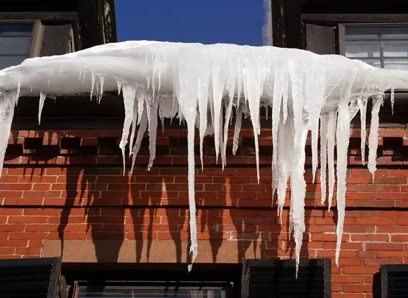 Thick icicles and an ice ridge hanging from a snow-loaded roof edge