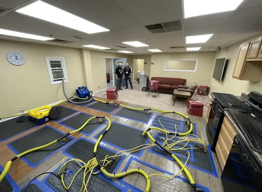 Drying mats, yellow hoses and air movers set across a wood floor